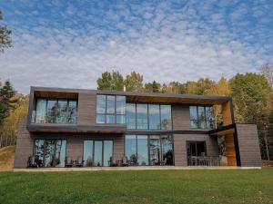 a large house with glass windows on a lawn at Le Ruisseau: luxurious villa in Charlevoix. in La Malbaie