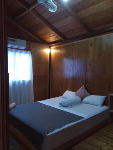 uma cama com almofadas brancas num quarto de madeira em Mentawai Bagus Local Homestay em Tua Pejat
