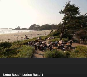 a beach with a long beach lodge resort and people sitting at tables at Forest Sweet Retreat Hot Tub & Wood Fired Sauna in Ucluelet