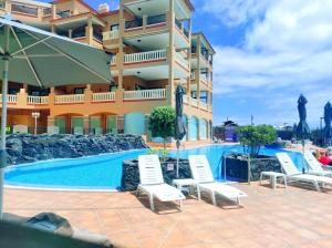 a hotel with a swimming pool with chairs and umbrellas at El Nautico Suites, Golf del Sur in San Miguel de Abona