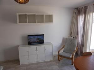 a living room with a tv on a white cabinet and a chair at Ático a 100 metros de la playa in Cullera