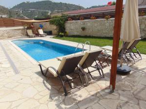 a swimming pool with chairs and an umbrella next to it at Charalambos Holiday Cottage in Kalavasos