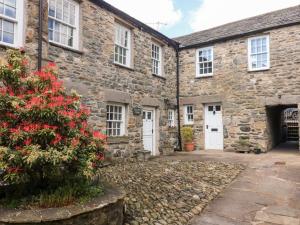 an old stone house with red flowers in front of it at Piggy Bank Cottage in Sedbergh