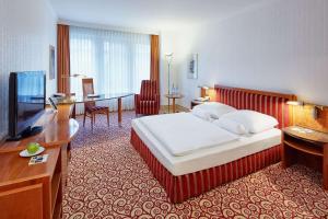 マクデブルクにあるDorint Herrenkrug Parkhotel Magdeburgのベッド、デスク、テレビが備わるホテルルームです。
