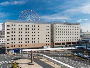 Un gran edificio blanco con una noria al fondo. en JR Kyushu Hotel Kagoshima, en Kagoshima