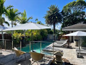 a swimming pool with chairs and umbrellas next to a house at Aabi's at Byron in Byron Bay