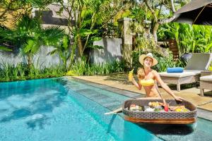 塞米亚克Mayaloka Villas Seminyak的坐在泳池旁一篮子食物中的比基尼女人