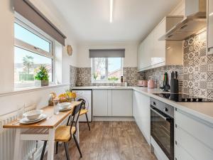 una cocina con armarios blancos y una mesa de madera con sillas. en The Beach Bungalow, en Beltinge