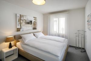 een slaapkamer met een bed met witte lakens en een raam bij Aparthotel Familie Hugenschmidt in Zürich