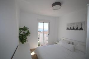 a white bedroom with a white bed and a window at Small Oasis Nelson Mandela Apartment with sea view, two bedrooms, parking, terrace and pool in Manilva