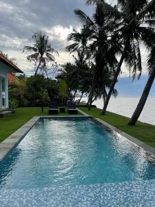 a swimming pool next to the ocean with palm trees at Mojito Beach Villas in Kubutambahan