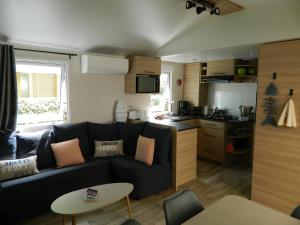 a living room with a black couch and a kitchen at Charmant mobil home 331 camping 4* Siblu La Réserve in Gastes