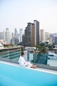 una mujer sentada en el borde de una piscina en un edificio en Public House Hotel - Sukhumvit 31, en Bangkok