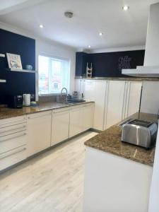 a kitchen with white cabinets and a wooden floor at Amazing Beach House, Sleeps 8, Pet Friendly in Trearddur