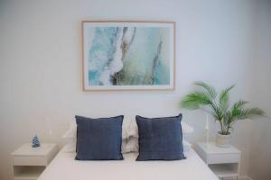 1 cama blanca con almohadas azules y una foto en la pared en SALTY SNOOZE - Your Coastal Holiday House en Avalon