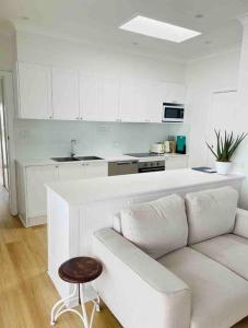 a white living room with a couch and a kitchen at SALTY SNOOZE - Your Coastal Holiday House in Avalon
