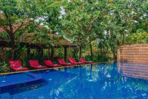 a swimming pool with red chairs and trees at Pandora Suite D'Angkor in Siem Reap