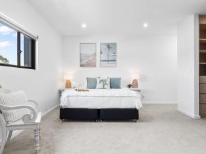 a white bedroom with a bed and a chair at Palmera on the south coast in Ulladulla