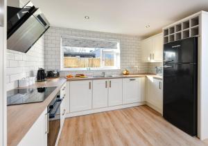 a kitchen with white cabinets and a black refrigerator at Maes Gwyn in Llanbedrog