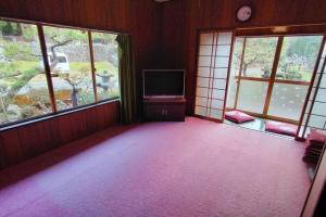 an empty room with a tv and two windows at 里山アウトドアフィールド・古民家コテージとろせ in Gujo