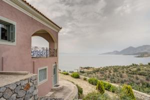 a pink house with a balcony overlooking the water at Filistron Seaview Guesthouse -Tranquil Coastal Gem in Taktikoúpolis