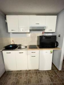 eine Küche mit weißen Schränken, einer Spüle und einer Mikrowelle in der Unterkunft Noclegi nad jeziorem w Puszczy Zielonka in Kamińsko