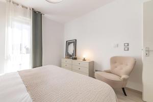 a white bedroom with a bed and a chair at OVELIA Les Angles - Les Loges d'Anicet in Les Angles Gard