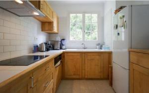 - une cuisine avec des placards en bois et un réfrigérateur blanc dans l'établissement Magnifique Maison avec piscine sans vis à vis 4 chambres et 1 mezzanine dans un milieu verdoyant, à Saint-Jean-du-Gard