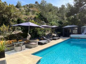 a swimming pool with couches and umbrellas next to a swimming pool at Villa en Provence, Spa & piscine, pour 9 personnes- Gîtes les Estelles in Cavaillon