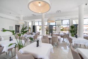 a restaurant with white tables and chairs and windows at Miramare Hotel in Zadar