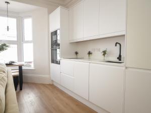 a white kitchen with white cabinets and a wooden floor at Fore Street House - Apartment 2 in Seaton