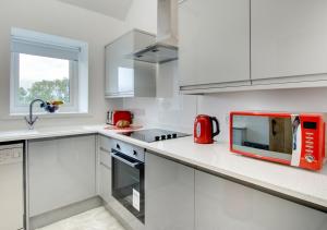 a white kitchen with a red microwave on the counter at Gwel y Cambria - Cambrian View in Rhostie