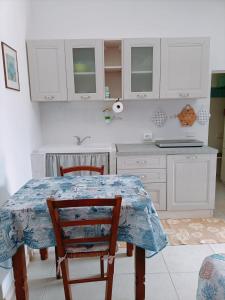 cocina con armarios blancos, mesa y sillas en Casa vacanza Ligustro appartamento il gabbiano, en SantʼAntìoco