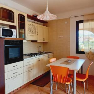 ヴィッラシミーウスにあるAppartamenti Il Glicine Villasimiusのキッチン(白いキャビネット、テーブル、オレンジの椅子付)