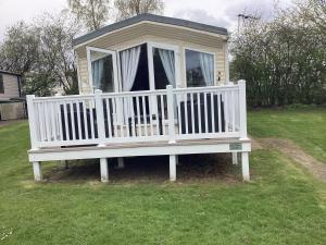 ein kleines Haus mit einer weißen Veranda auf dem Rasen in der Unterkunft Luxury caravan at Seton Sands in Port Seton