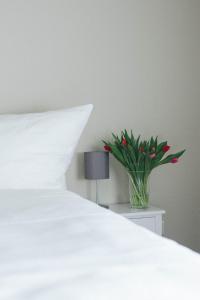 a white bed with a vase of red flowers on a night stand at Landhaus Begatal in Dörentrup