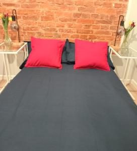 a bed with two red pillows next to a brick wall at Hola Apartamenty Legionow in Łódź