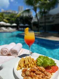 a plate of food and a drink next to a pool at Mar Hotel Conventions in Recife