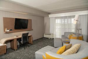 a hotel room with a couch and a desk with a television at Courtyard by Marriott Erie Ambassador Conference Center in Erie