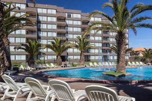 a resort pool with white chairs and palm trees at Hotel Club La Serena in La Serena