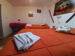 dwa łóżka w pokoju z pomarańczową pościelą w obiekcie Hostal Raymi w mieście Ollantaytambo