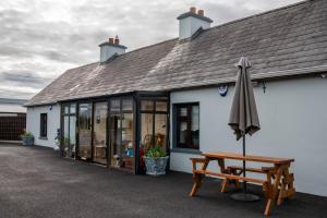 a white building with an umbrella and a bench at Sheila's Cottage Ballyheigue in Ballyheigue