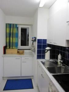 uma cozinha com armários brancos, um lavatório e azulejos azuis em Chasa Triazza em Scuol