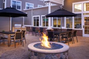 eine Feuerstelle auf einer Terrasse mit Tischen und Sonnenschirmen in der Unterkunft Residence Inn by Marriott Saginaw in Saginaw