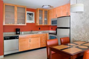 a kitchen with wooden cabinets and a table and a refrigerator at Residence Inn by Marriott Houston The Woodlands/Lake Front Circle in The Woodlands