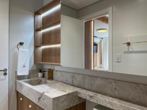 y baño con lavabo de mármol y espejo. en Apartamento Res Aire 3 Suítes by Achei Gramado, en Gramado