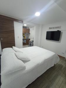 1 dormitorio con 1 cama blanca y TV de pantalla plana en Apartaestudio con 2 camas cerca al centro y parqueadero GRATIS en Popayán