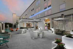 un patio al aire libre con mesas, sillas y sombrillas en Aloft Austin Round Rock en Round Rock