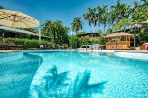 a swimming pool with an umbrella and chairs and trees at Palms City Resort in Darwin