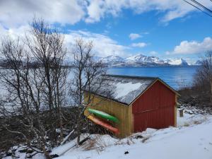 a redshed with snow on it next to a lake at Senja Skaland in Melkarhola